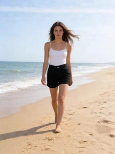 Women's summer outfit with white camisole and black high waisted denim shorts on beach