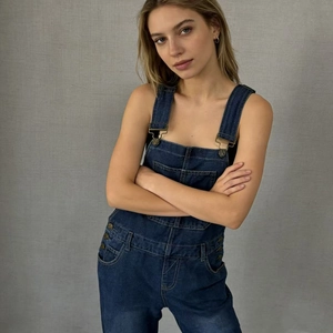 Détails de la salopette en jean bleu foncé avec boucles en bronze et grande poche frontale