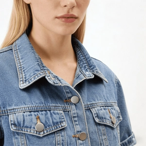 Detailansicht von hellblauem Jeansjackenkragen mit Metallknöpfen und Steppnähten