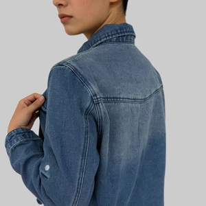 Detail view of washed denim jacket with back horizontal seam and white button cuff