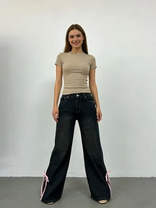 Dettaglio dei jeans neri a vita alta a gamba larga con fiocchi di nastro rosa sull'orlo laterale