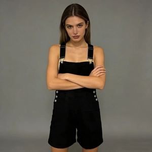 Detailed view of black denim overalls with silver metal buckles and side button accents