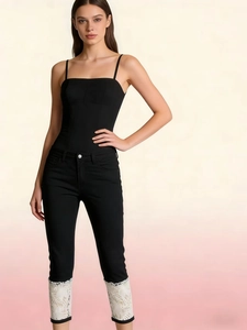 Close-up of black slim cropped pants with elegant white floral lace trim at the hem