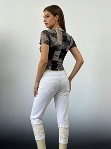 Detailed view of white cropped jeans featuring elegant floral lace trim at the bottom hem