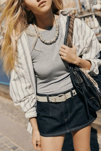 Dettaglio di gonna in denim blu scuro con cintura bianca e borsa a mano in pelle nera