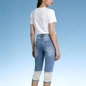 Detail of light blue denim pants featuring elegant white floral lace stitching on the hems