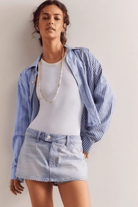 Dettaglio della minigonna in denim lavaggio chiaro con bordi sfrangiati e camicia blu