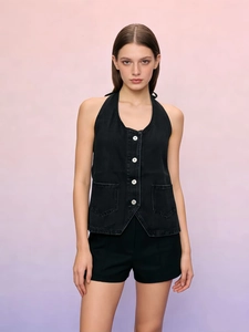 Detail of black denim halter vest featuring white contrast buttons and functional side pockets