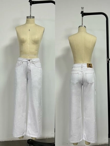 Detail view of white straight-leg denim jeans showing cherry logo leather patch and five pockets