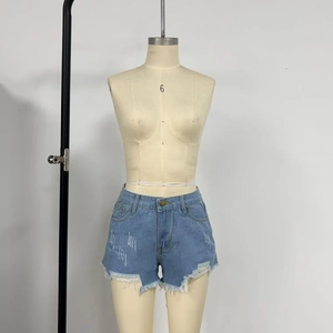 Detail of high-waist denim shorts with distressed rips, frayed hems and metal buttons