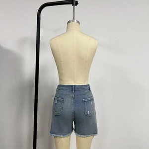 Detail of mid-waist blue denim shorts featuring distressed back pockets and frayed hems