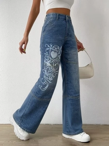 Détails d'un jean bleu large à taille haute avec motifs de cœurs et vignes blancs