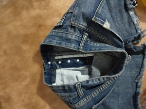 Close-up of ripped blue denim shorts featuring five metal buttons and distressed fringes