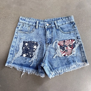 Detail of distressed denim shorts featuring American flag patchwork and frayed edges