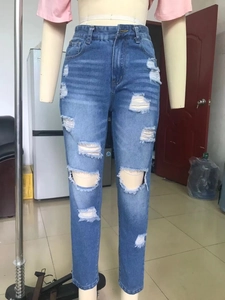 Detail of high waisted blue skinny jeans with distressed ripped knees and raw edge texture