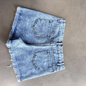 Detail view of denim shorts with acid wash finish and frayed hems on gray background