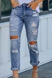 Detailed view of light blue distressed denim jeans with frayed holes and rolled-up cuffs