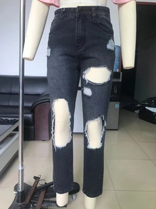 Detail of high waisted distressed denim jeans in dark grey with ripped knee accents