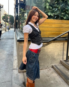 Détail du gilet en jean sur chemise blanche avec ceinture rouge et jupe longue en jean