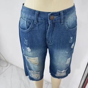 Detail of distressed dark blue denim shorts with ripped holes and branded metal button