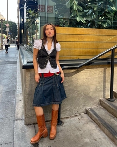 Détail d'un gilet en jean noir ajusté avec chemise blanche et ceinture rouge femme