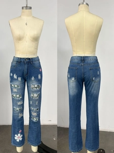 Detail of ripped light blue jeans with floral patch inserts and flower print on the hem