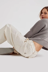 Dettaglio dei pantaloni cargo avorio con tasche laterali e fibbia metallica sul maglione a coste