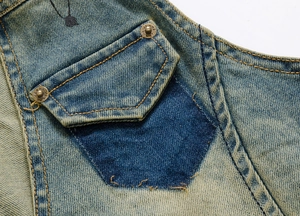 Close-up of washed blue denim vest with contrast stitching, metal rivets, and print detail