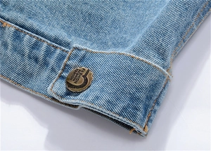 Détail macro du gilet en jean bleu clair avec bouton en métal et coutures orange vif