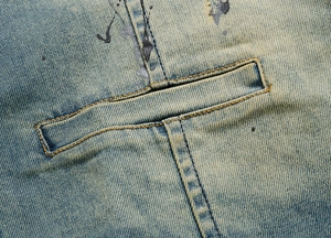 Detail of light blue washed denim fabric with yellow stitching and paint splatters