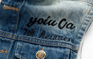 Detail of blue denim vest with black embroidery and vintage engraved metal button