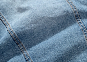 Détail de tissu denim bleu clair avec double surpiqûre orange et texture délavée