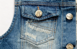 Detail of denim vest with brass button featuring engraved logo and classic stitching