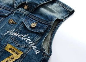 Dettaglio del gilet in denim blu scuro con ricamo bianco e bottoni in metallo con marchio