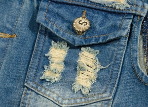 Detail of flap pocket with metal button and distressed ripped denim fabric on vest