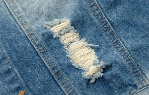Macro detail of blue denim vest featuring distressed ripped holes and orange contrast stitching