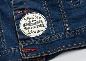 Close-up of deep blue denim jacket featuring red stitching, metal rivets and a round patch
