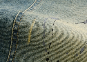 Macro shot of light blue denim fabric with distressed splattered paint and double stitching