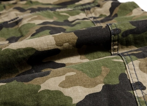 Detailed close-up of jungle camouflage fabric with reinforced double stitching on denim vest