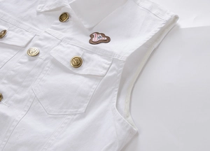 Dettaglio del gilet di jeans bianco con bottoni in metallo e toppa ricamata