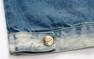 Close-up of distressed blue denim vest fabric with bronze SUDHIR logo metal button