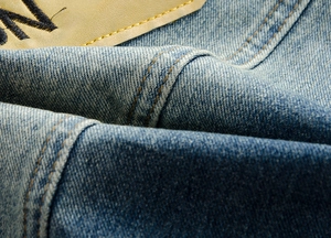 Dettaglio ravvicinato del tessuto denim azzurro con etichetta in pelle e ricamo