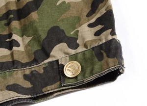Detailed close-up of camouflage denim vest featuring a golden embossed metal button