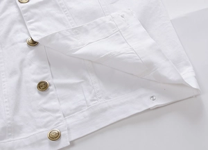 Dettaglio dell'orlo del gilet di jeans bianco con bottoni in bronzo incisi e trama twill