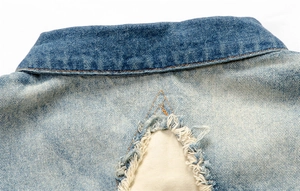 Close-up of distressed denim vest collar with frayed edges and yellow stitching