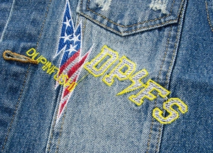 Detail of blue denim vest featuring premium embroidery with DRIES lettering and lightning bolt