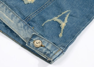 Macro detail of washed blue denim vest featuring A-shaped distressed hole and metal button