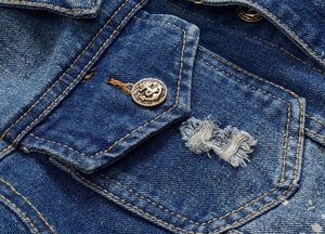 Close-up of distressed blue denim jacket featuring anchor embossed metal buttons