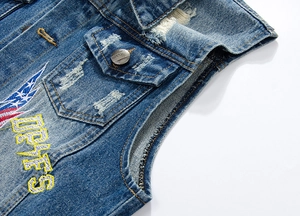 Detail of blue denim vest featuring vintage embroidery and distressed frayed edges