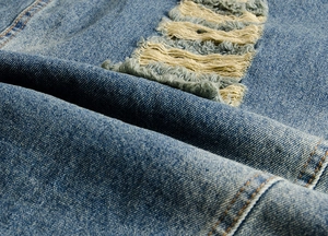 Detail of distressed denim fabric featuring ripped texture and yellow stitching on blue vest